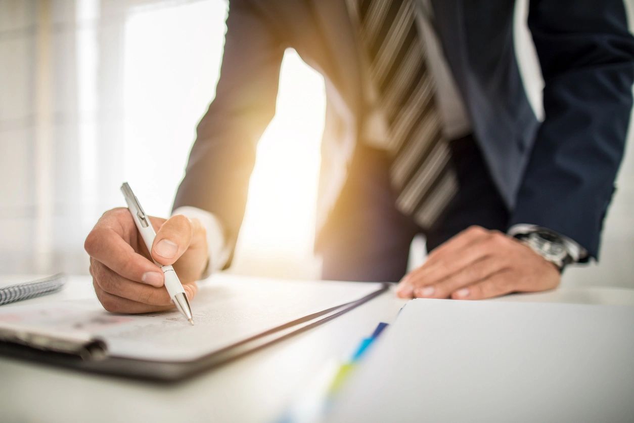 A person in suit writing on paper next to another person.